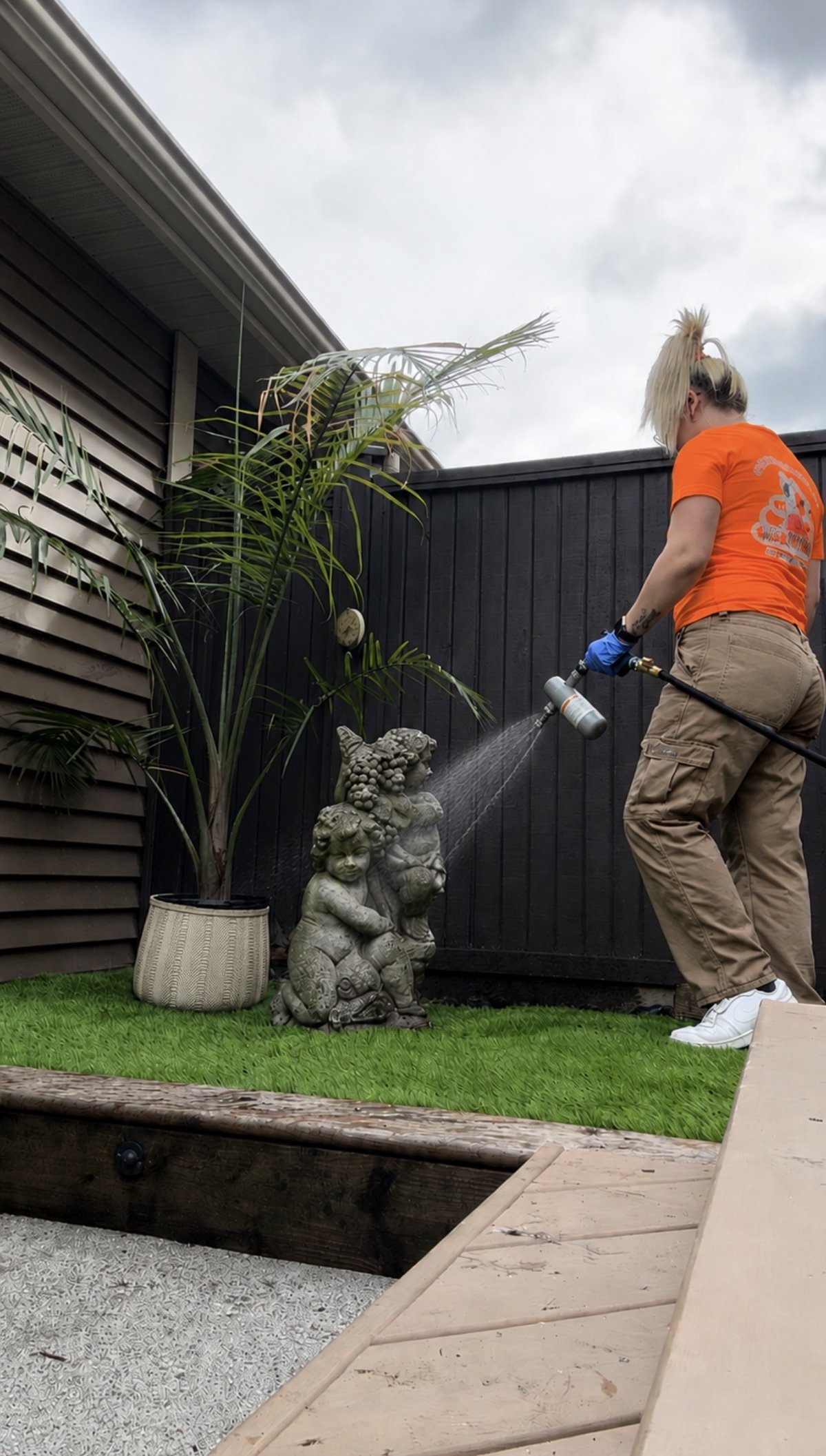 Kira from Woof Waste applying a pet-safe deodorizing spray in a client's yard
